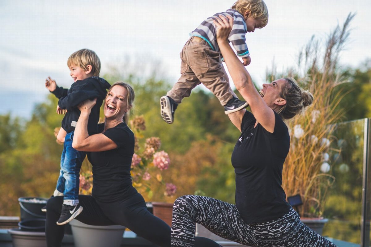Zwei Frauen heben ihre Kleinkinder beim Training auf der Terrasse