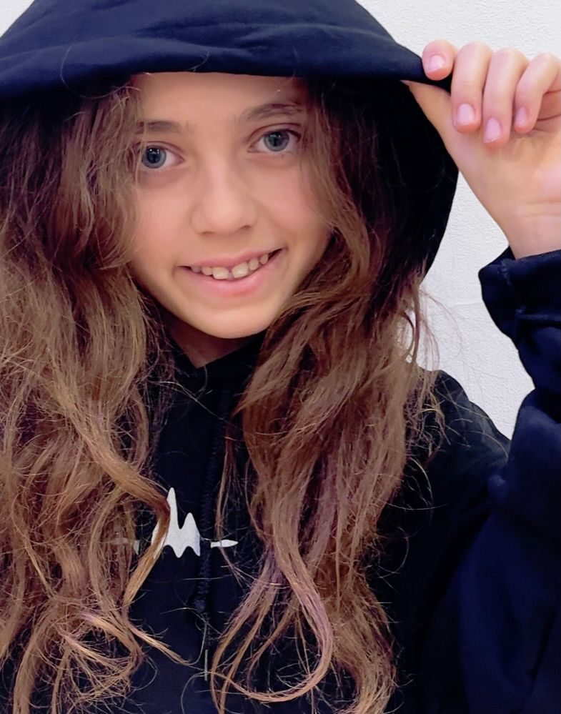 Mädchen mit langen Locken in einem Studio-Hoodie mit Kapuze