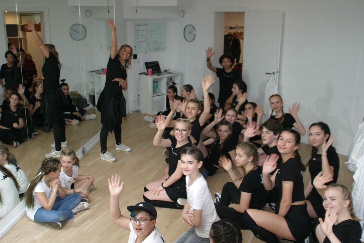 Große Kindergruppe sitzt im Studio und winkt in die Kamera