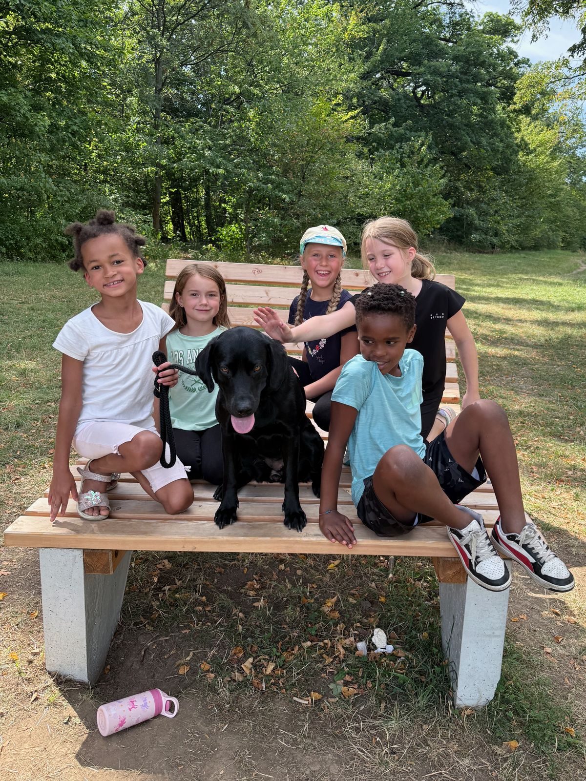 Fünf Kinder mit einem schwarzen Hund auf einer Bank